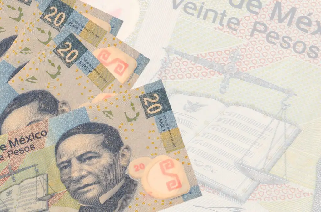 "Embrace It" Tourist Tax 2026 2 Several Mexican 20 peso banknotes with a portrait of Benito Juárez, partially overlapping on a faded background showing scales of justice and an open book.